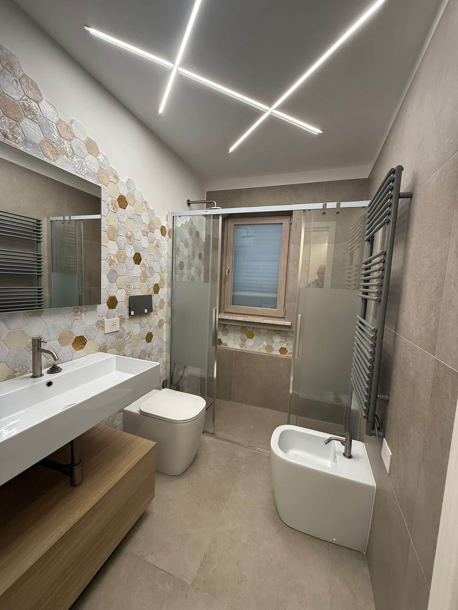 A modern bathroom with a large mirror, two sinks, a shower enclosure, and a toilet.
