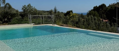 A clear swimming pool with a metal structure in the middle, surrounded by greenery and hills.