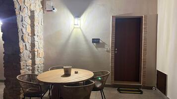 Ein Zimmer mit einer Steinsäule, einem runden Holztisch mit Stühlen, einer Tür und einer Wandleuchte.