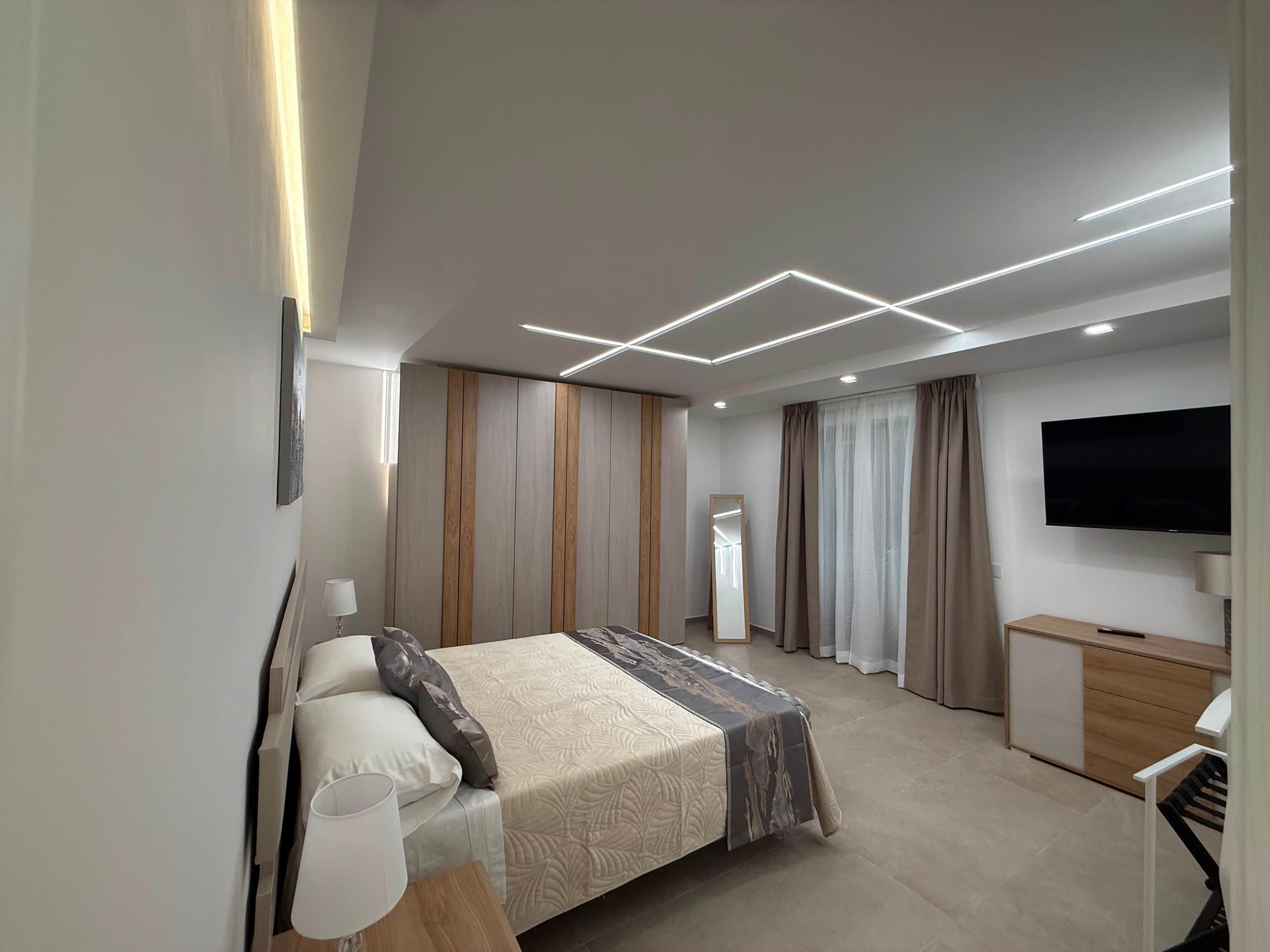 Una moderna camera d'albergo con un letto, comodino, lampada, televisione e una scrivania con una sedia.