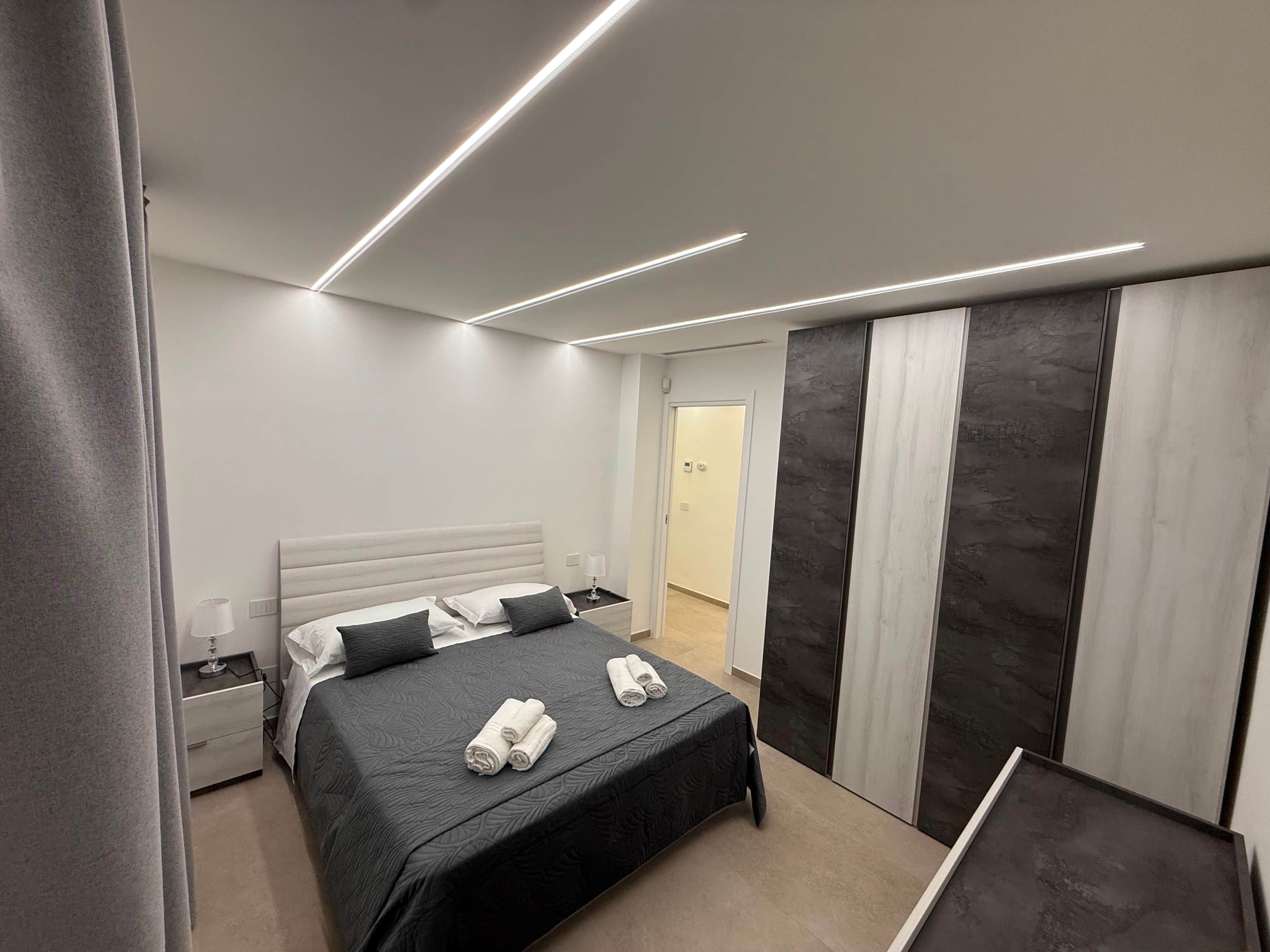 Une chambre d’hôtel moderne, équipée d’un lit, de tables de chevet, d’une petite table et d’une porte donnant sur une autre pièce.