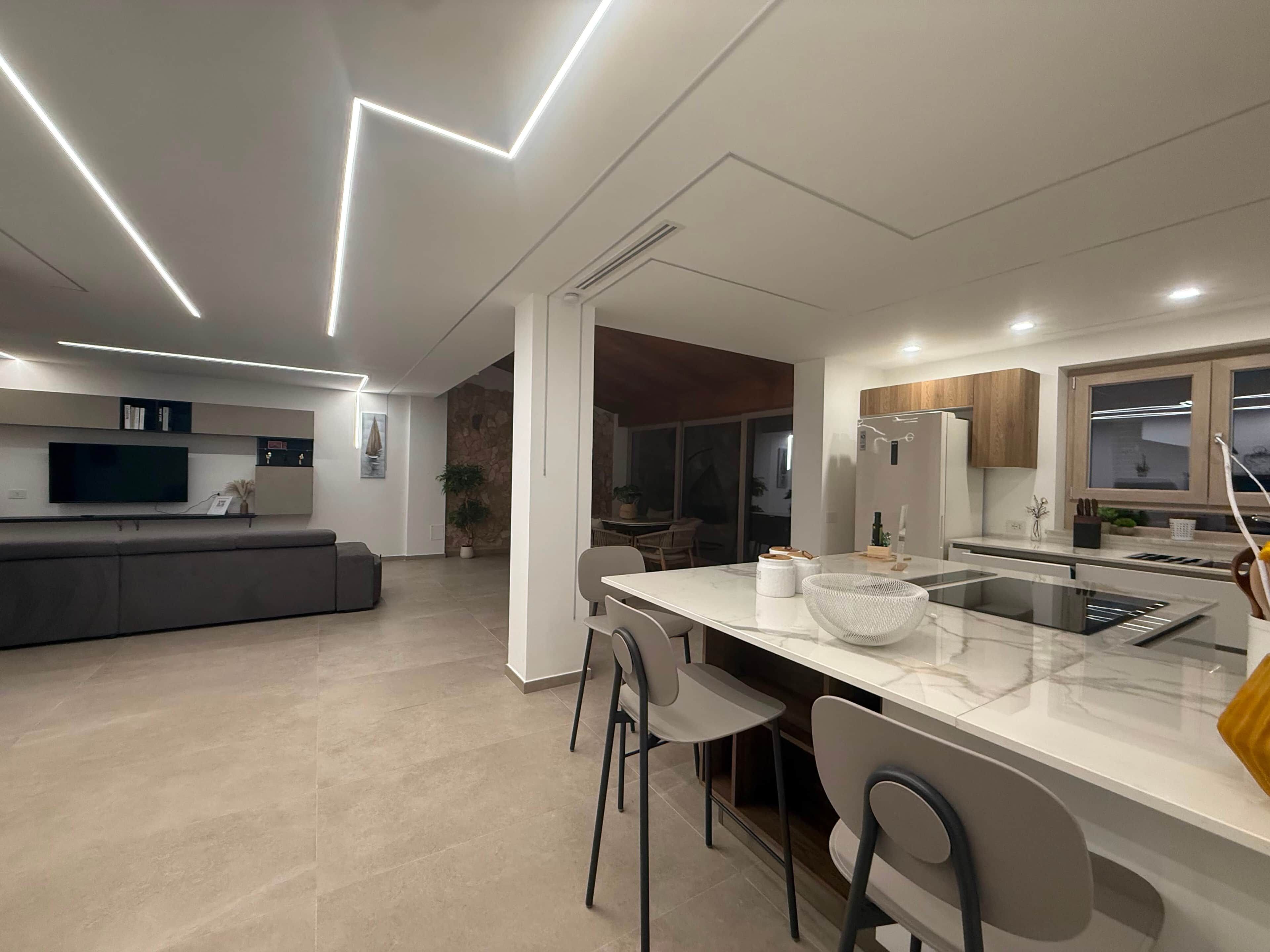 Una cucina moderna con isola centrale, zona pranzo con sedie e angolo living con divano e TV.