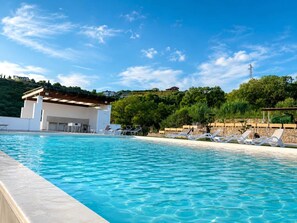 A swimming pool with lounge chairs, a covered area, and a view of a hillside with buildings. - Villa Heaven Relax (Lazio)