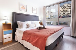 Ein modernes Hotelzimmer mit einem großen Bett, Nachttischen, einem Fenster mit Blick auf Gebäude und einem Balkon.