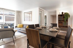 Ein moderner Essbereich mit einem Marmortisch, schwarzen Stühlen und einer Couch im Hintergrund.