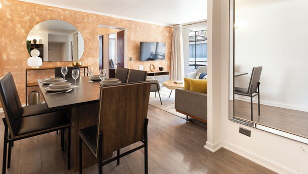 Een moderne woonkamer met een eethoek, een grote spiegel en een televisie.
