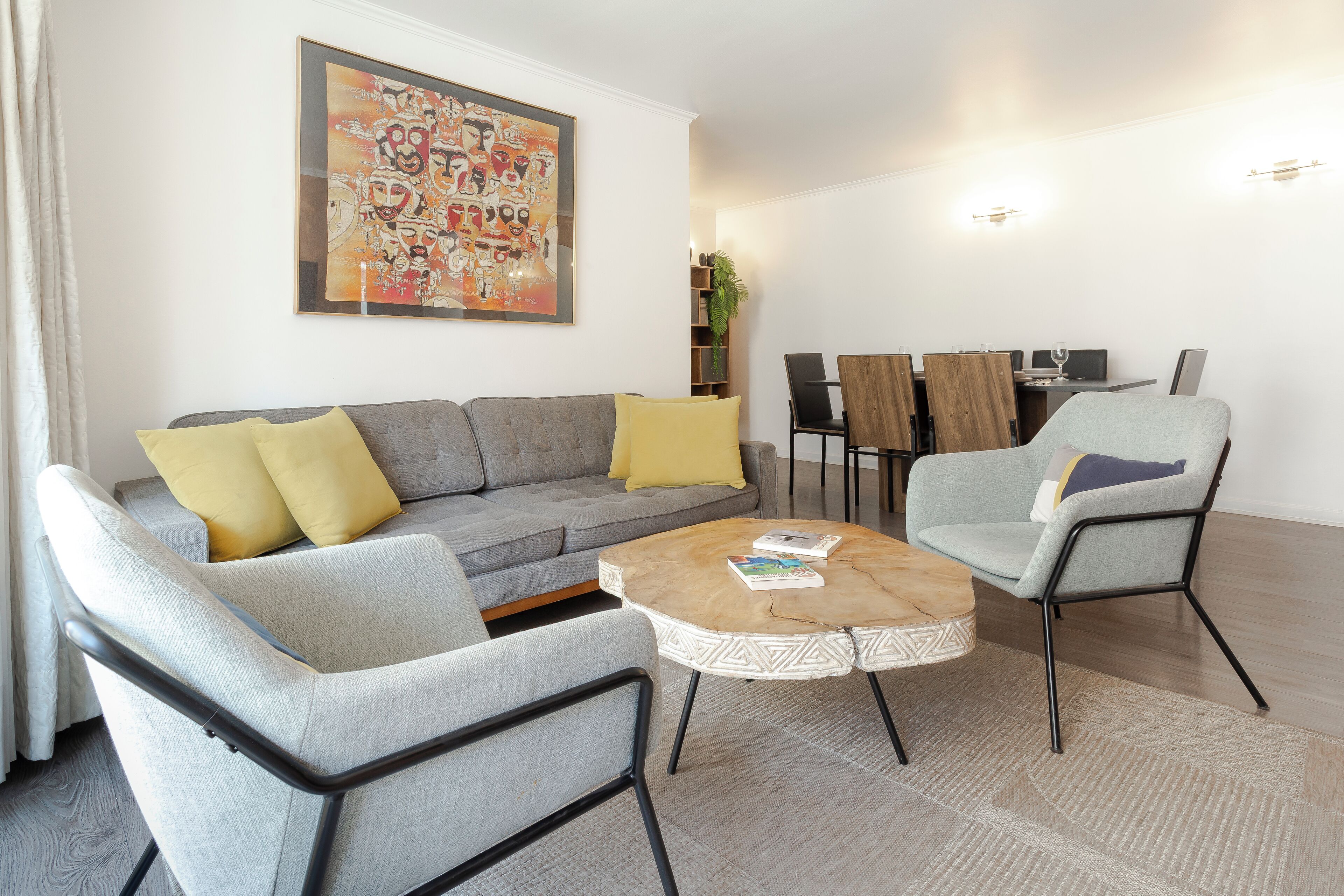 A modern living room with a grey sofa, two armchairs, a coffee table, and a dining area with a wooden table and chairs.