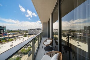 Un balcon avec des fauteuils en osier et une table, d’où l’on peut admirer un paysage urbain avec ses bâtiments et une route.
