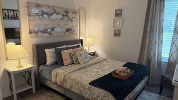 Un dormitorio con cama, mesitas de noche, lámpara, espejo y ventana con cortinas.