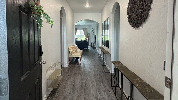 Un couloir avec une porte en bois sombre, un banc, un élément décoratif mural et une vue sur un espace de vie comprenant un canapé et un téléviseur.