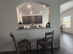 A kitchen with dark cabinets, a microwave, and a window with blinds. There are two chairs in front of the kitchen.