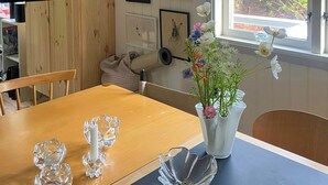 A dining area with a wooden table, clear glass candle holders, a vase with flowers, and framed artwork on the wall.