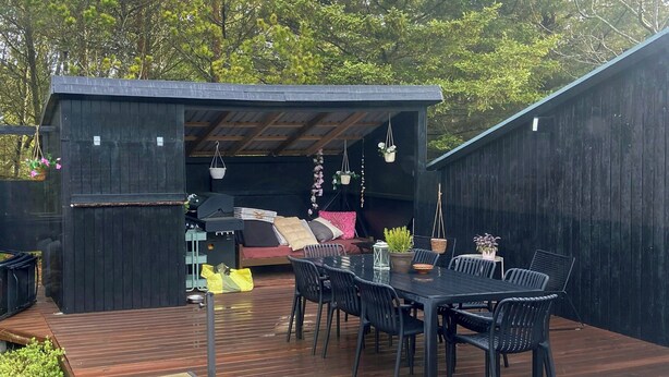 A covered outdoor patio with a table and chairs, a grill, and hanging plants.