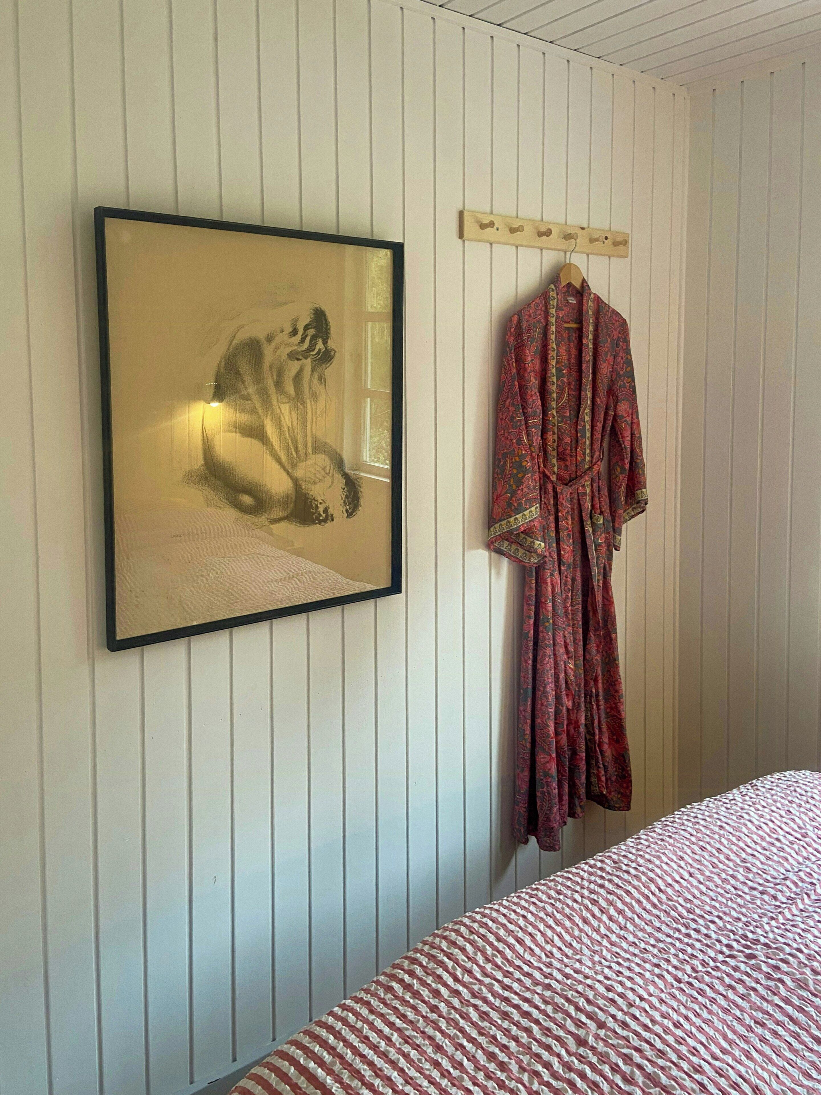 Une chambre à coucher avec un lit, une œuvre d’art encadrée et un peignoir suspendu à un porte-manteau.