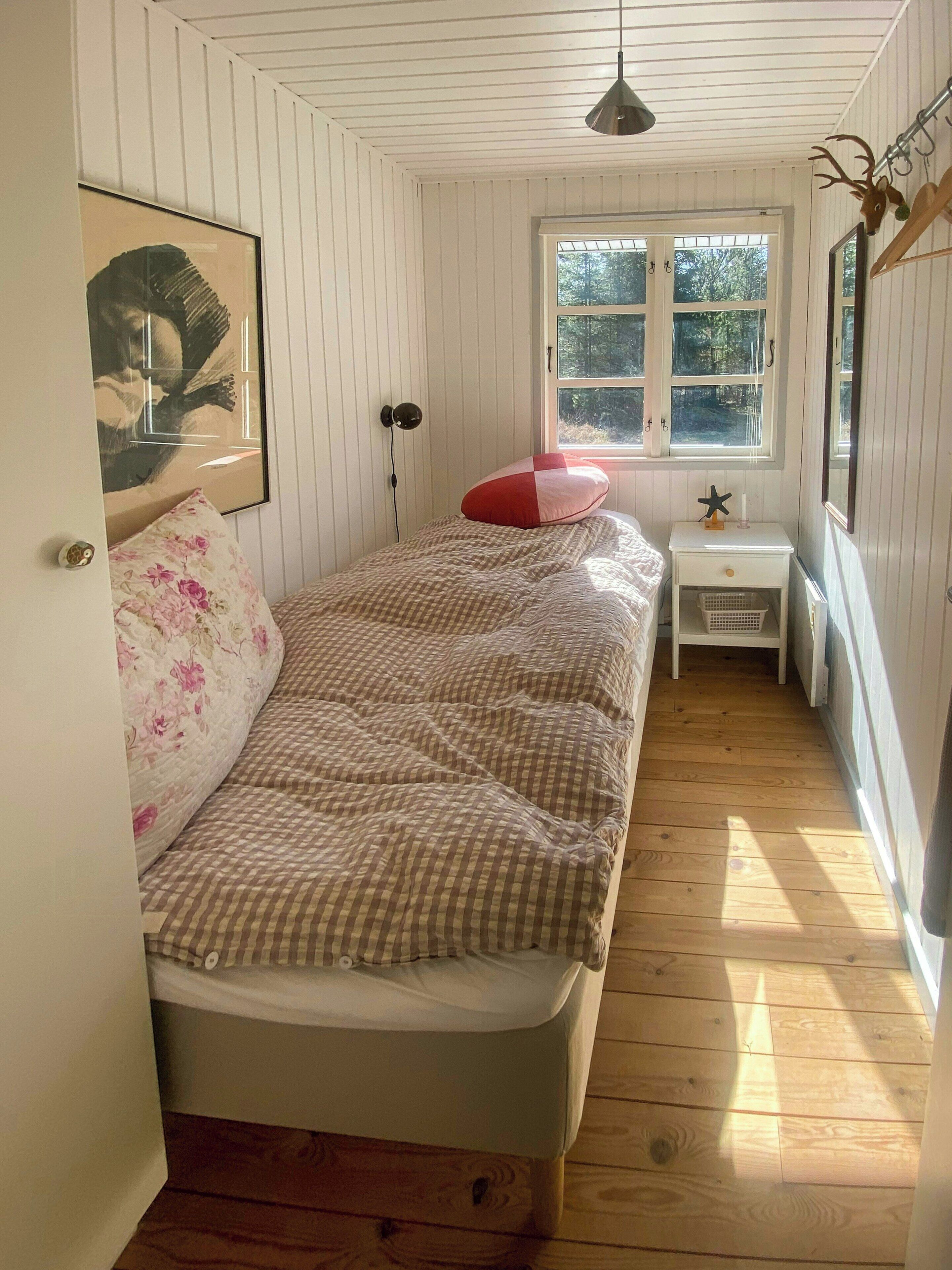 Ein Schlafzimmer mit Bett, Fenster, Nachttisch und Wandlampe.