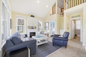 Ein geräumiges Wohnzimmer mit Kamin, einer Treppe und einer Tür mit der Aufschrift 'Beach'.