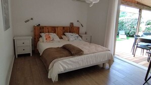 Een slaapkamer met een houten bed, witte wanden, een plafondventilator en uitzicht op het omliggende landschap.