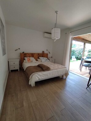 Ein Schlafzimmer mit einem hölzernen Bett, weißen Wänden, einem Deckenventilator und Blick ins Freie.