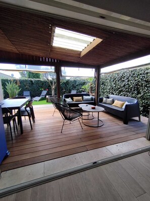 Eine Außenpatio-Terrasse mit Holzboden, einer Sitzecke, einem Esstisch mit Stühlen und einem kleinen runden Tisch.