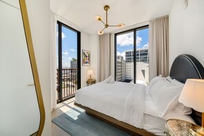 Ein Hotelzimmer mit einem großen Bett, einem Balkon, Blick auf die Stadt und einer modernen Pendelleuchte.