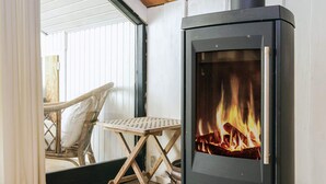 A room with a black wood-burning stove, a wicker chair, and a small table. - 4 Star Holiday Home in Gorlev (Gørlev)