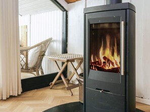 Una habitación con un estufa de leña de madera oscura, una silla de mimbre y una pequeña mesa.