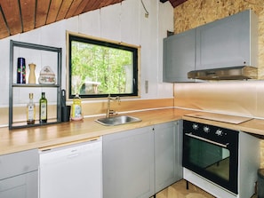 Una cocina con lavavajillas, horno y ventana con vista a árboles.