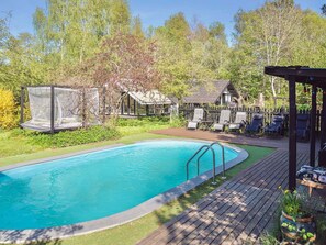 Una piscina con terraza de madera, sillas de descanso y un área de estar cubierta.