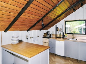 Una cocina con techo de madera, armarios blancos, encimera de madera, un fregadero y una ventana.
