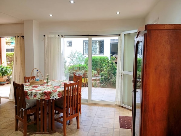 A dining area with a table set for four, wooden chairs, a water bottle, and a vase with flowers.