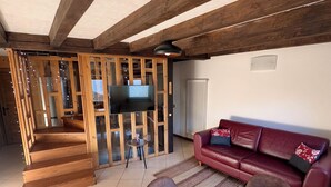 A spacious living area with a wooden staircase, a red leather sofa, a TV, and a dining table with chairs.