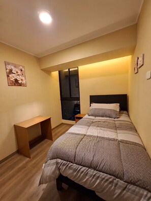 Ein Schlafzimmer mit Bett, Nachttisch, Sitzbank, Fenster und Deckenleuchte.