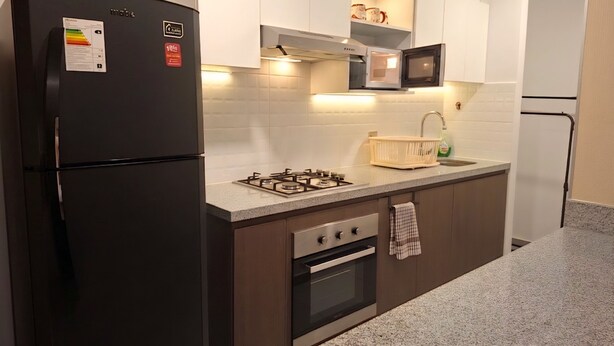 A modern kitchen with a black refrigerator, gas stove, oven, and white cabinets. - 3 bedroom apartment (Lima)