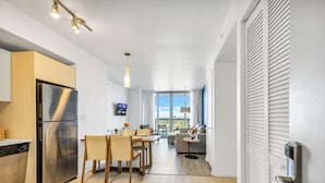 A modern kitchen with a built-in refrigerator, dining area with chairs and a table, and a living room with a sofa and a TV. - Intracoastal Panorama- 2BR Beachwalk Resort (Hallandale Beach)