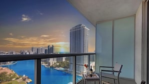 A balcony with a view of a city skyline, a body of water, and a table with a bottle and glasses. - Intracoastal Panorama- 2BR Beachwalk Resort (Hallandale Beach)
