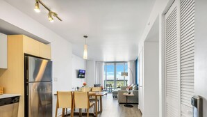 A modern kitchen with a stainless steel refrigerator, wooden cabinets, and a dining area with a table and chairs. - High-Floor 1BR - Intracoastal View - Resort & Pool (Hallandale Beach)
