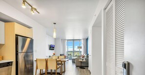 Eine moderne Küche mit einem Edelstahl-Kühlschrank, eine Essecke mit Tisch und Stühlen, einem wandmontierten Flachbildfernseher und einem großen Fenster mit Blick.