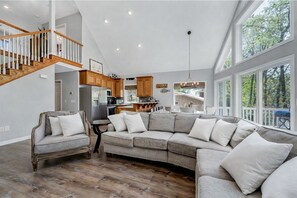 Ein geräumiger Wohnbereich mit einem großen, grauen Ecksofa, einer Holztreppe und einer Küche mit Holzausstattung.