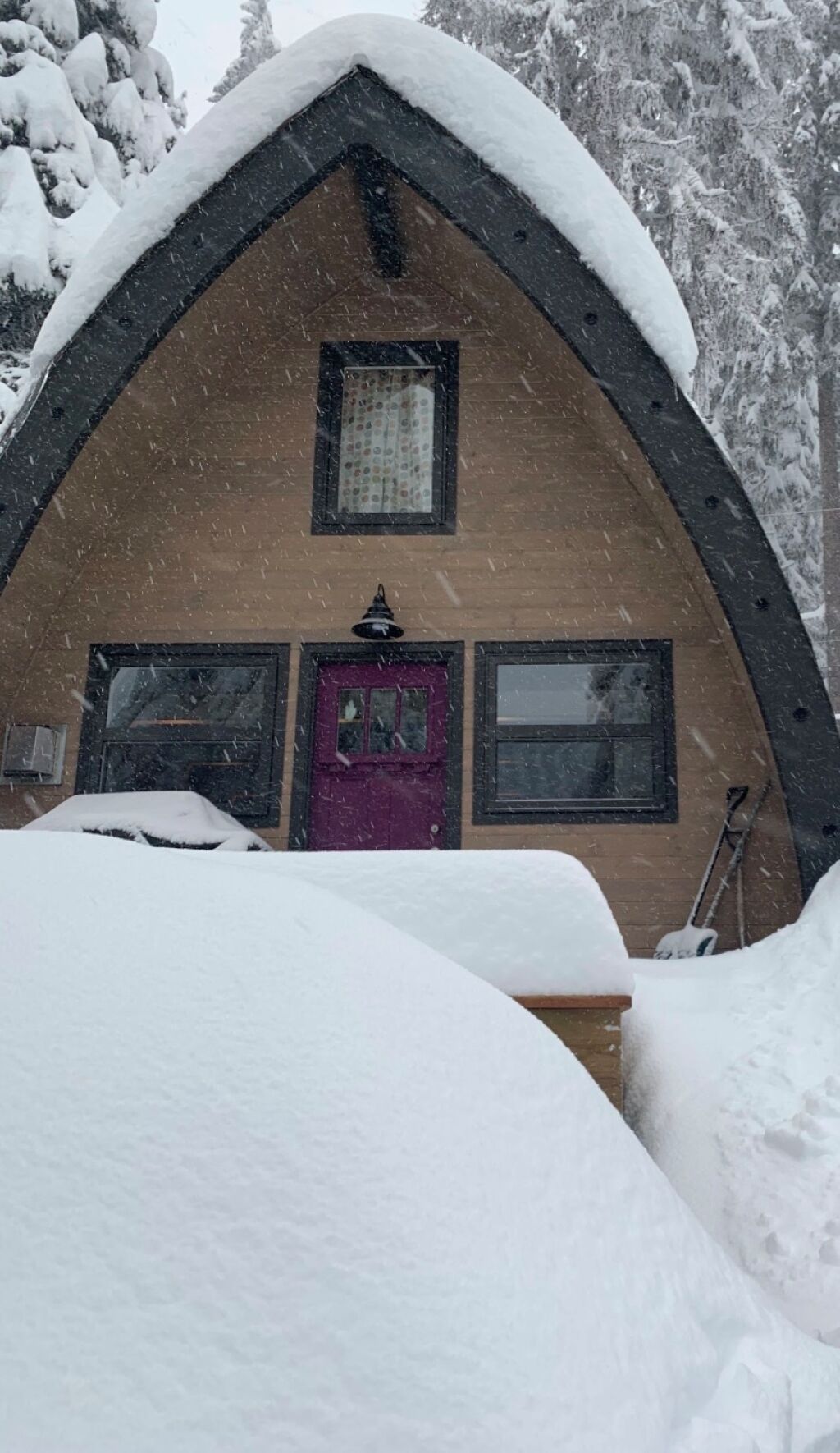 Une cabane en bois recouverte de neige, avec un toit à deux versants, une porte visible et des fenêtres.