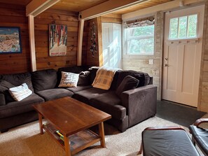 A cozy cabin interior with a brown sofa, a wooden coffee table, and a door with a window. - Popular Cabin Colony - steps from village, hot tub (Silver Star Mountain)