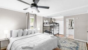 Ein Schlafzimmer mit einem Bett, Deckenventilator, einem Etagenbett, einem Nachttisch und einem Teppich.