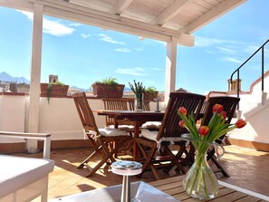 Una terrazza esterna con tavolo e sedie, un vaso con fiori e vista sulla città.
