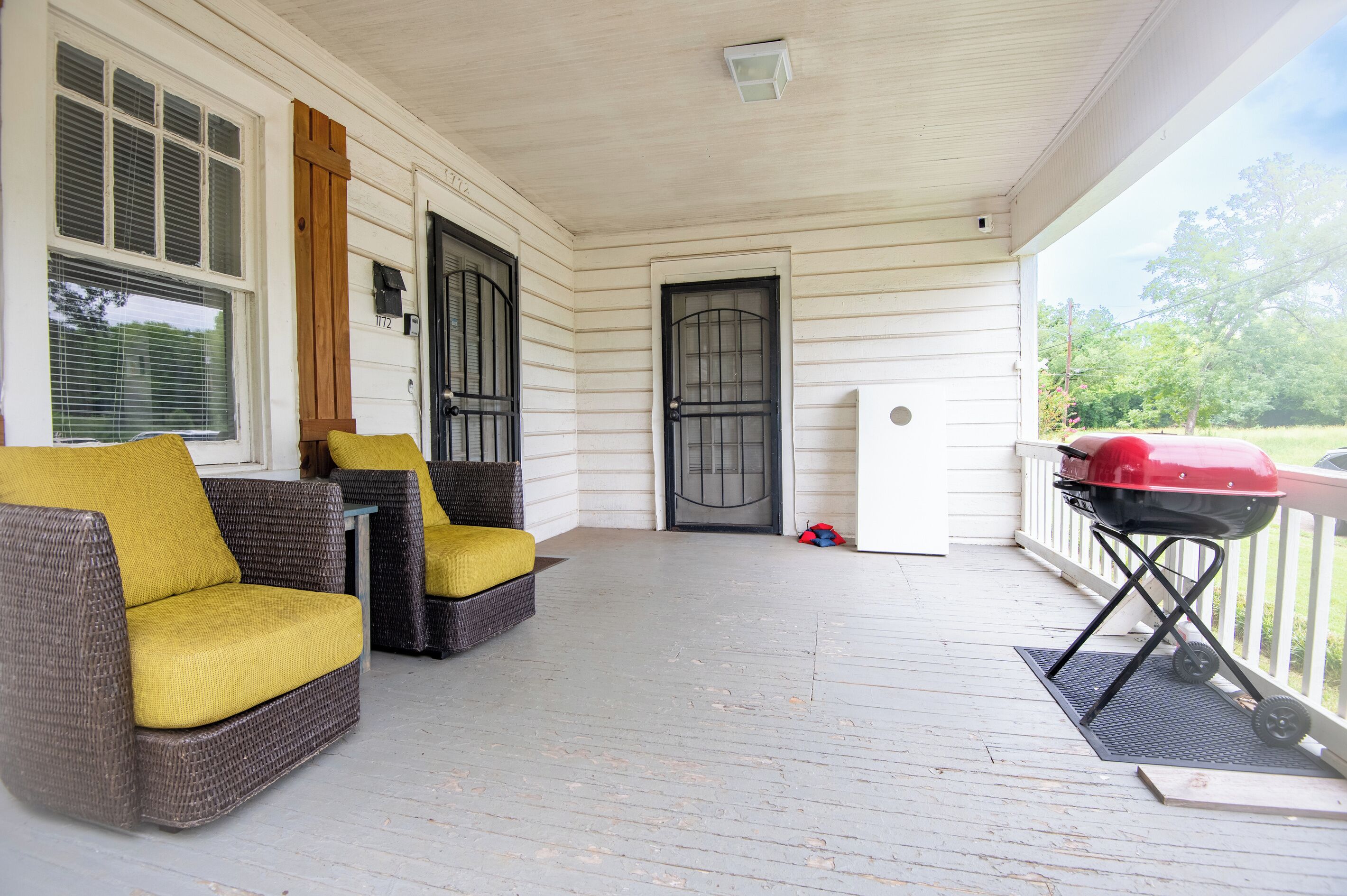 A covered porch with wicker furniture, a grill, and a door with a window.
