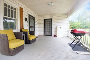 A covered porch with wicker furniture, a grill, and a door with a window.