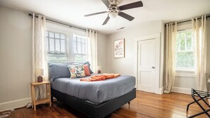 Ein Schlafzimmer mit Bett, Deckenventilator, Fenster mit Jalousien und einer Tür.