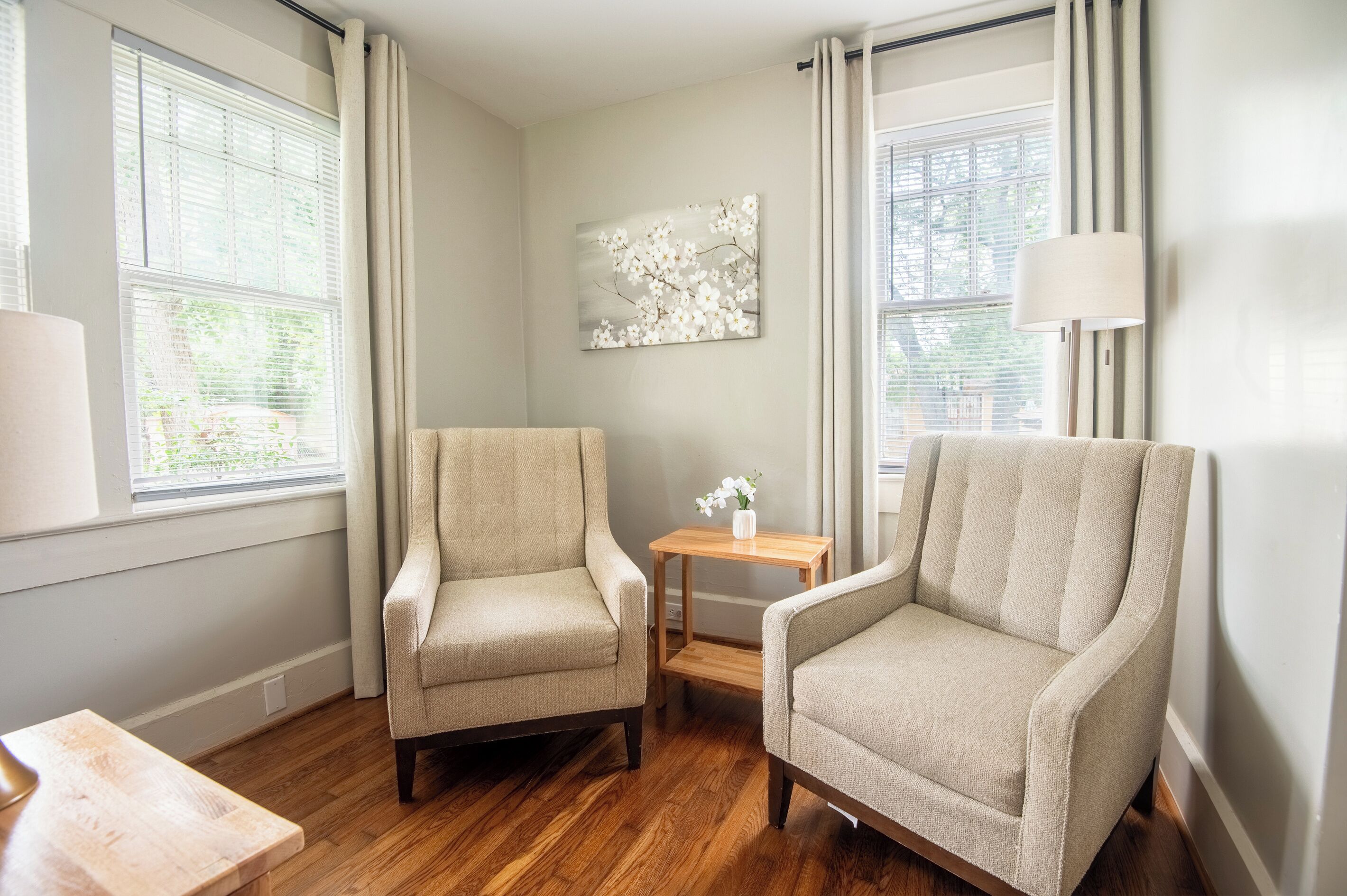 A room with two armchairs, a small table with a vase, and a painting on the wall.