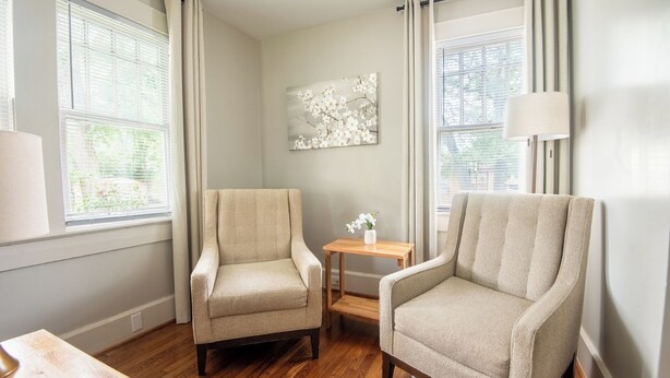 Ein Zimmer mit zwei Sesseln, einem kleinen Tisch mit einer Vase und einem Gemälde an der Wand.