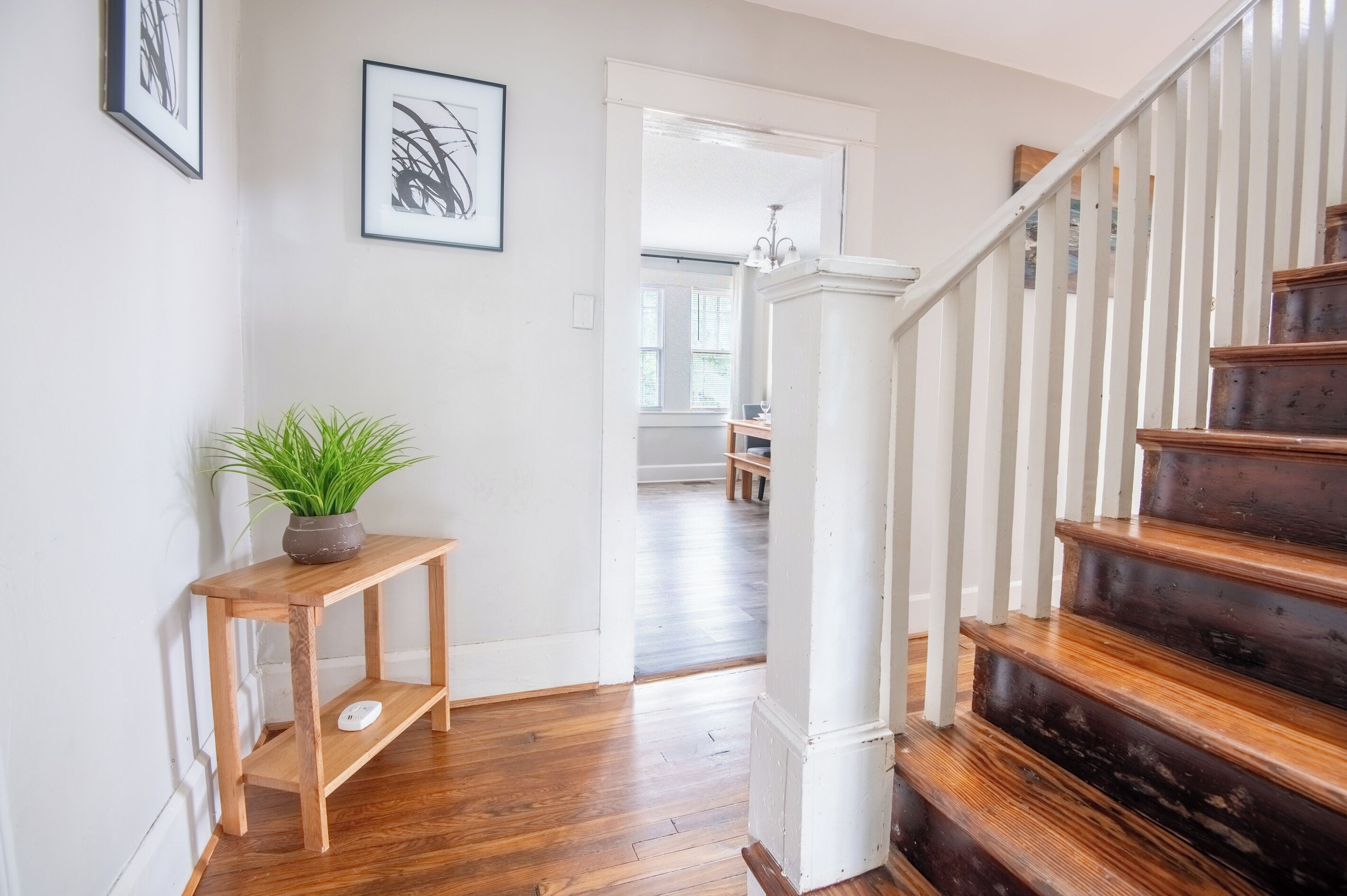 A wooden staircase with white railings leading to an upper floor. A potted plant is placed on a small wooden table beside the staircase.