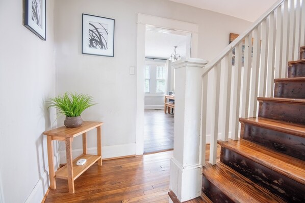 A wooden staircase with white railings leading to an upper floor. A potted plant is placed on a small wooden table beside the staircase.