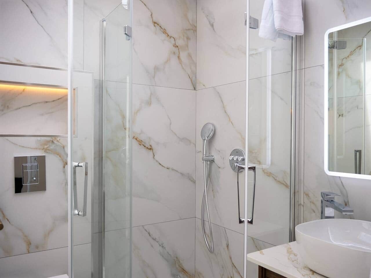 Une salle de bain moderne avec une douche à parois de verre, un lavabo blanc et un mur recouvert de carreaux de marbre.